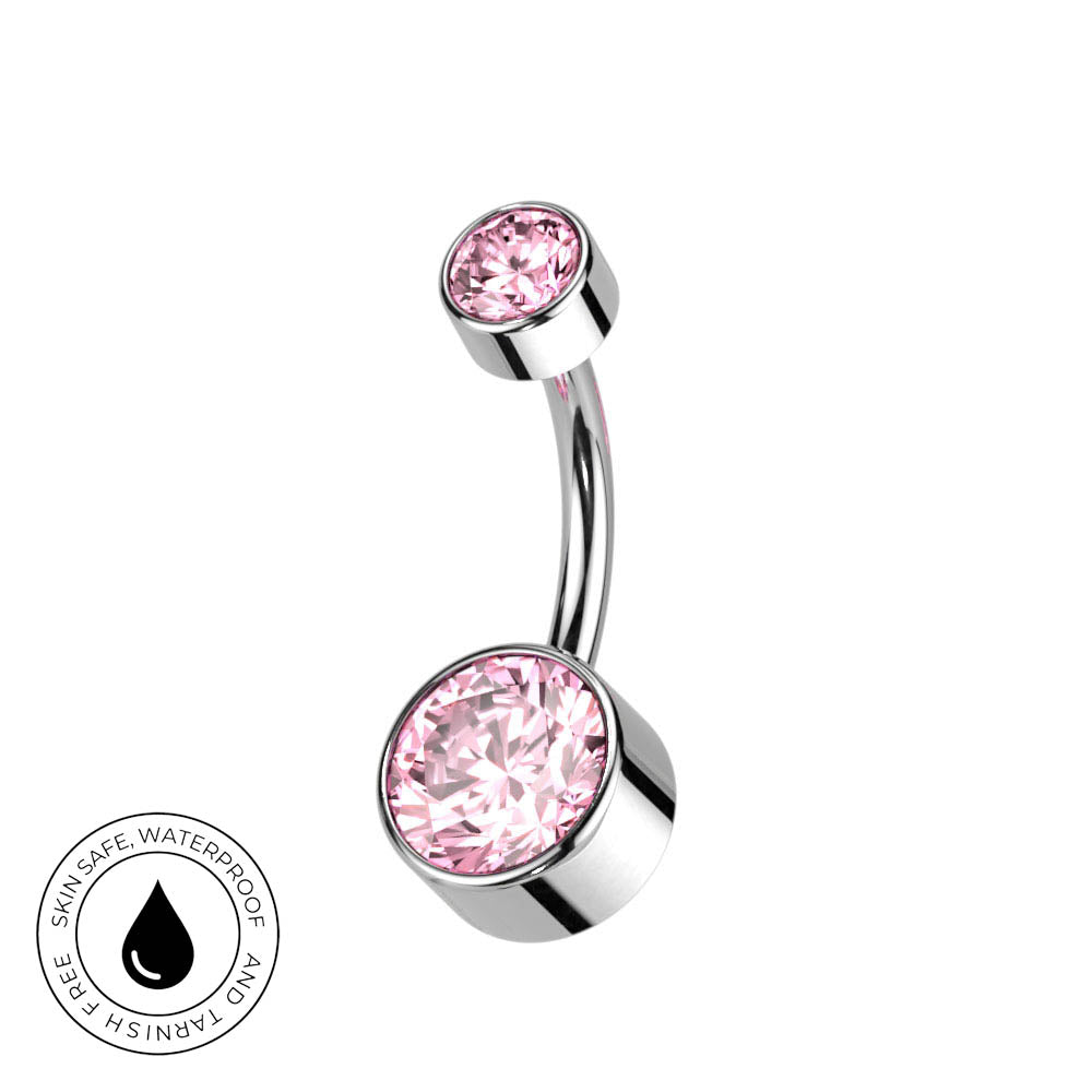 A curved barbell belly button ring with a large round pink crystal and a smaller pink crystal on a polished silver-tone metal, shown on a white background with a circular 'Skin Safe Waterproof' badge in the lower left.
