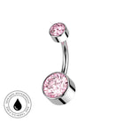 A curved barbell belly button ring with a large round pink crystal and a smaller pink crystal on a polished silver-tone metal, shown on a white background with a circular 'Skin Safe Waterproof' badge in the lower left.