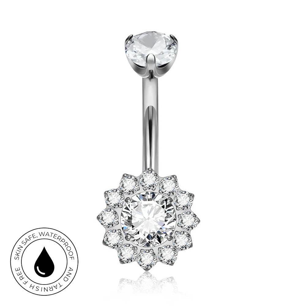 Silver-toned navel ring with a single round clear gemstone at the top and a flower-shaped halo of smaller clear gemstones at the bottom, shown on a white background with a circular skin-safe waterproof badge in the lower left.