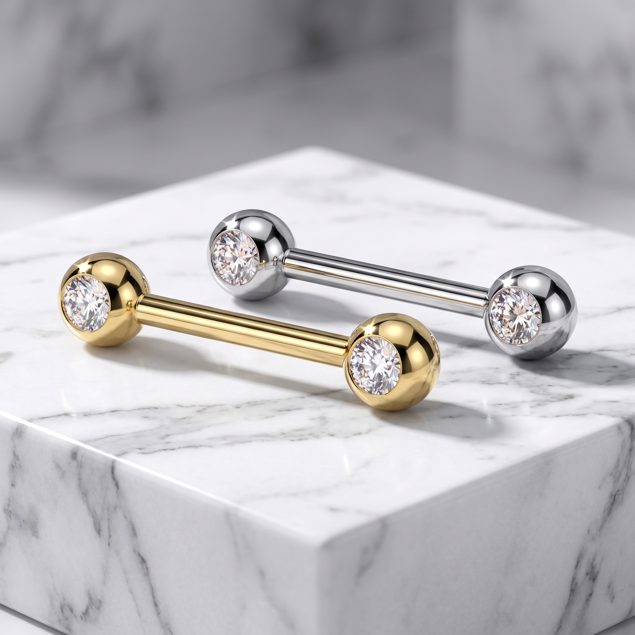 Two barbell stud earrings displayed on a white marble block. One earring is gold-toned with a clear gemstone, and the other is silver-toned with a clear gemstone.