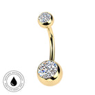 Gold curved barbell navel jewelry with two round bezel-set clear gemstones, shown on a white background with a circular 'Skin Safe Waterproof' badge in the lower left.