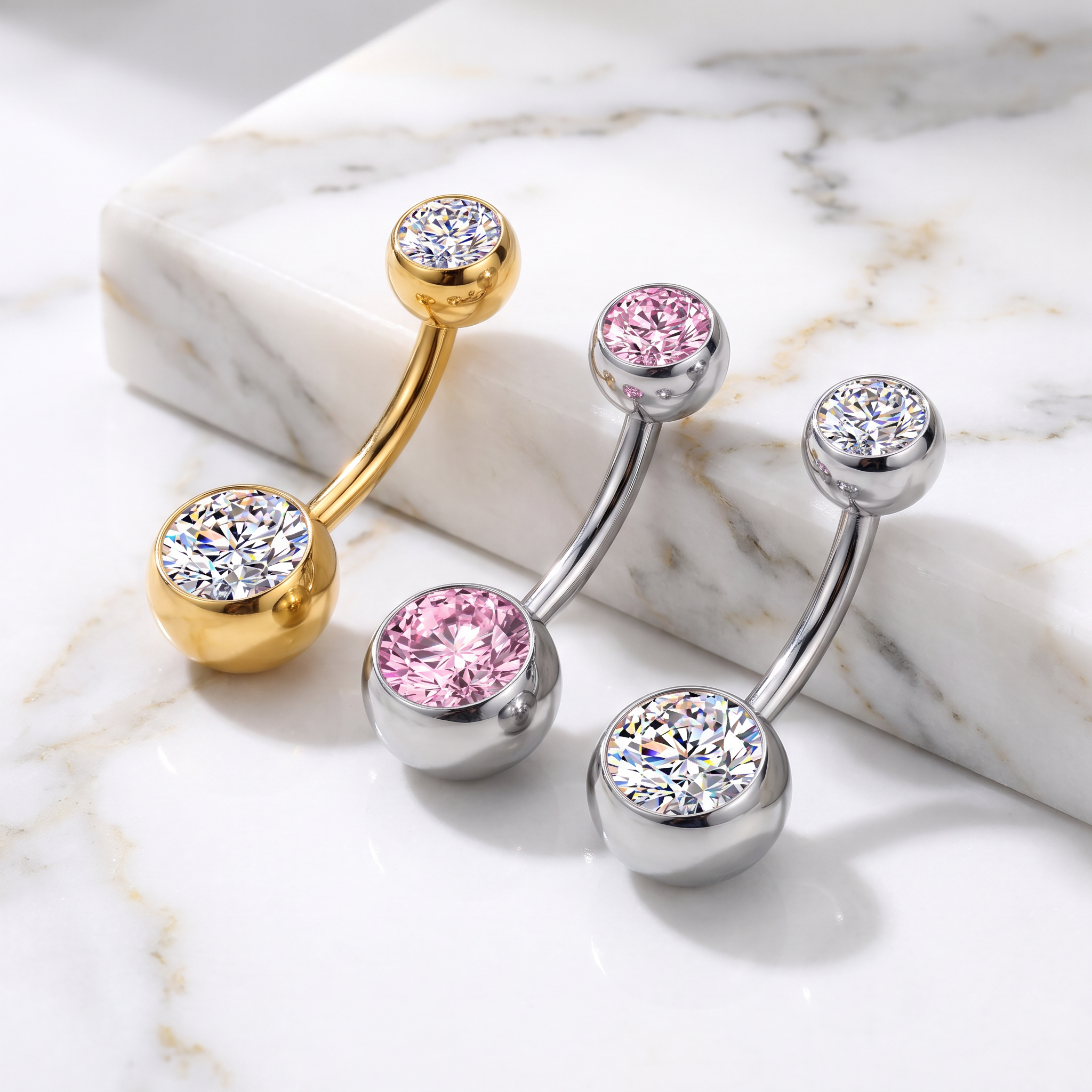 Three curved barbell belly button piercings with round gemstone settings are arranged on a white marble slab. One piece is gold-toned with a clear stone, and two silver-toned pieces are each accented with a pink gemstone.