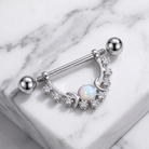 A silver-toned curved barbell piercing jewelry piece with a central iridescent opal-like stone and small clear stones, displayed on a white marble surface.