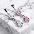 Silver-toned curved barbell belly button jewelry with pink and clear gemstones, displayed on a white marble block.
