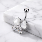 A silver belly button ring featuring a butterfly design with white mother-of-pearl heart wings and clear rhinestone accents, displayed on a white marble block over a white marble surface.