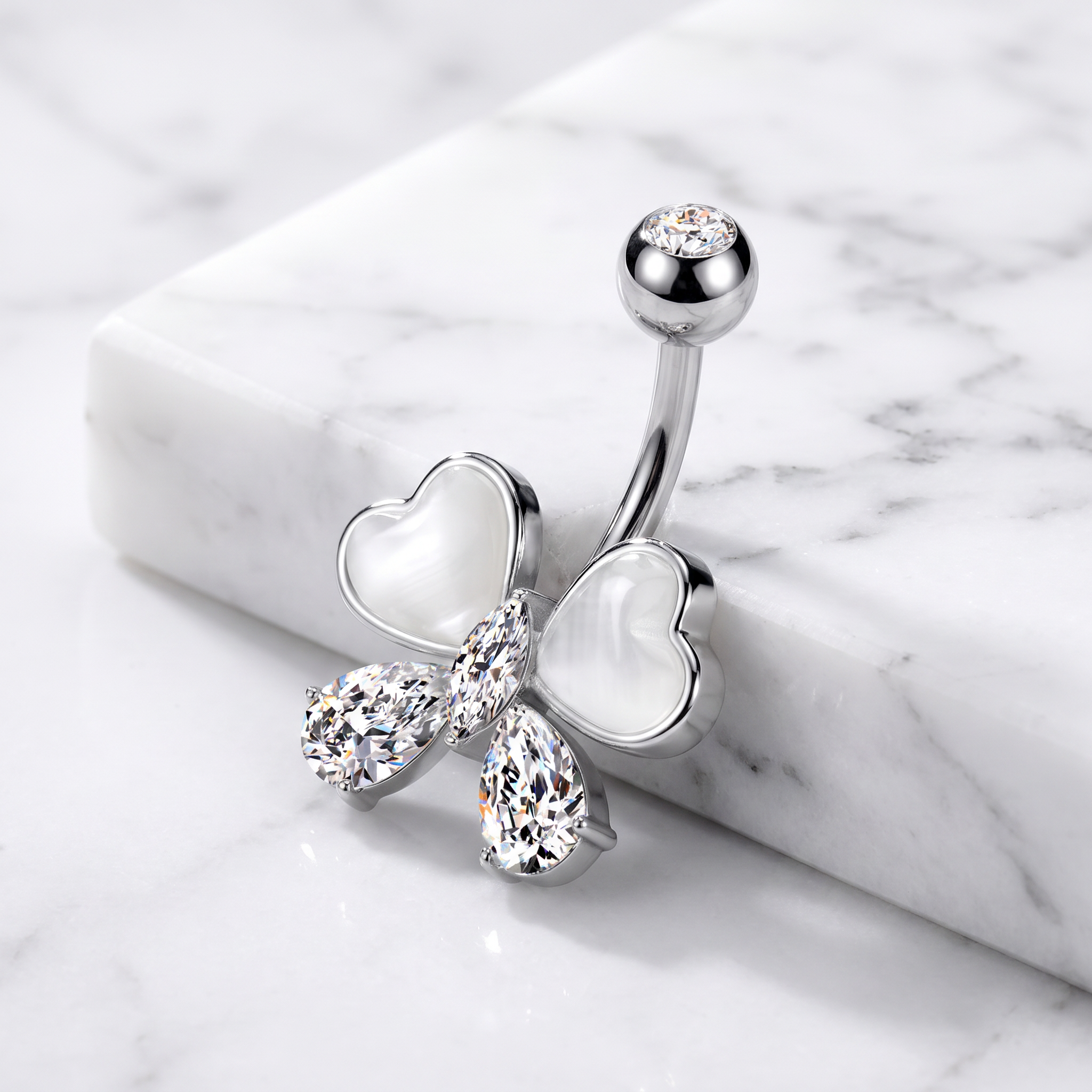 A silver belly button ring featuring a butterfly design with white mother-of-pearl heart wings and clear rhinestone accents, displayed on a white marble block over a white marble surface.