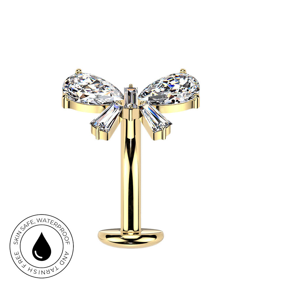 A gold nose stud featuring a bow-shaped setting with clear marquise and baguette gemstones, shown on a plain white background with a circular 'Skin Safe Waterproof' badge in the lower-left corner.