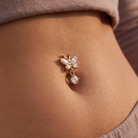 A gold butterfly-shaped belly button ring with clear gemstones, shown worn on a person's navel.