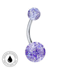 A curved barbell navel piercing jewelry piece with two round glittery purple and white marbled beads on a silver-tone metal bar, shown on a white background with a circular skin-safe waterproof badge in the lower-left corner.