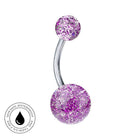 A curved barbell navel piercing jewelry piece with two glittery purple and pink spheres on a silver-tone metal bar, shown on a white background with a circular skin-safe waterproof badge in the lower-left corner.
