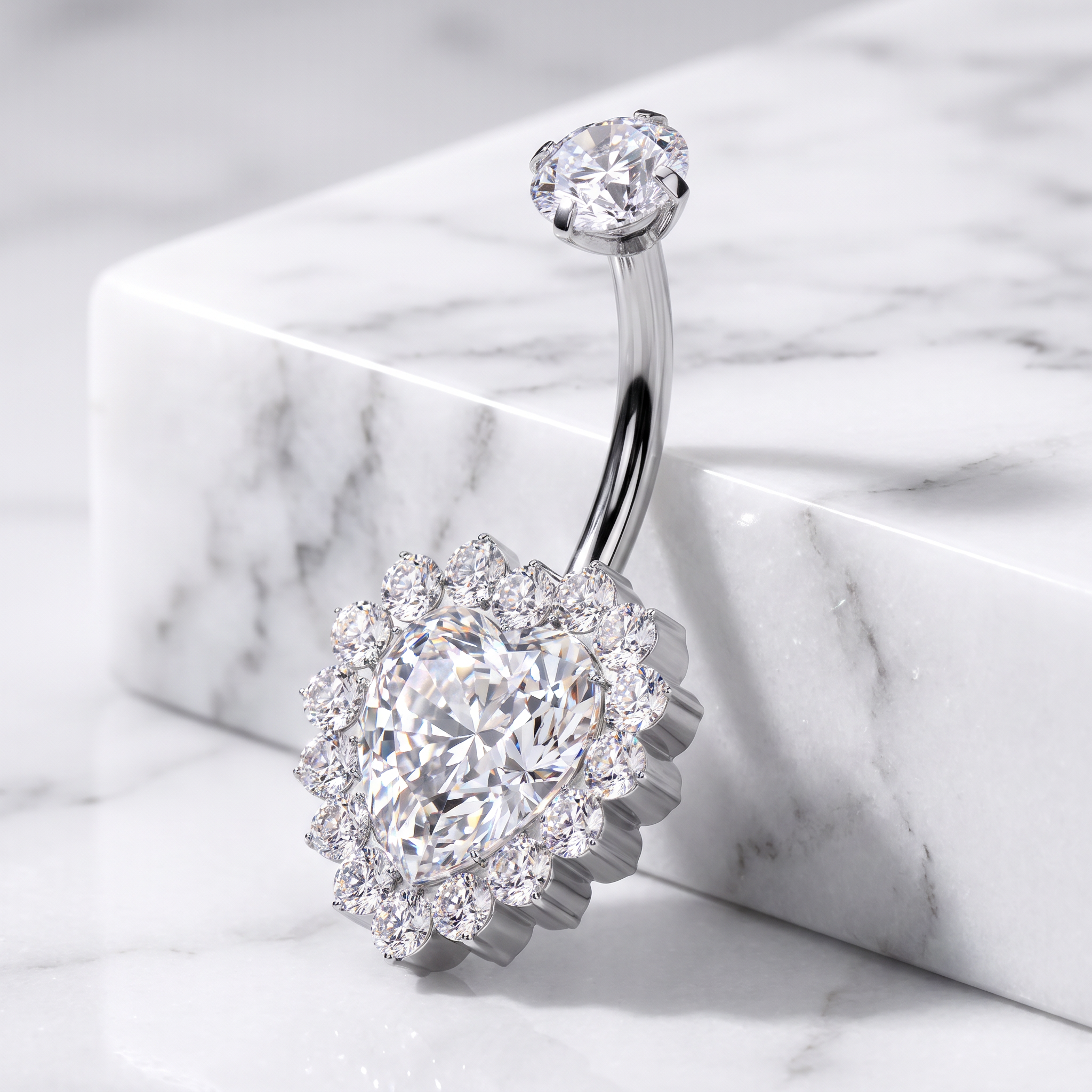 A silver-toned belly button ring with a large marquise-cut clear gemstone surrounded by a halo of smaller clear stones, resting on a white marble block against a white marble surface.