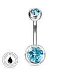 A silver-toned barbell navel piercing jewelry piece featuring a large faceted light blue gemstone on the bottom ball and a smaller matching blue gemstone on the top ball, shown on a white background with a circular 'Skin Safe Waterproof' badge in the lower left.
