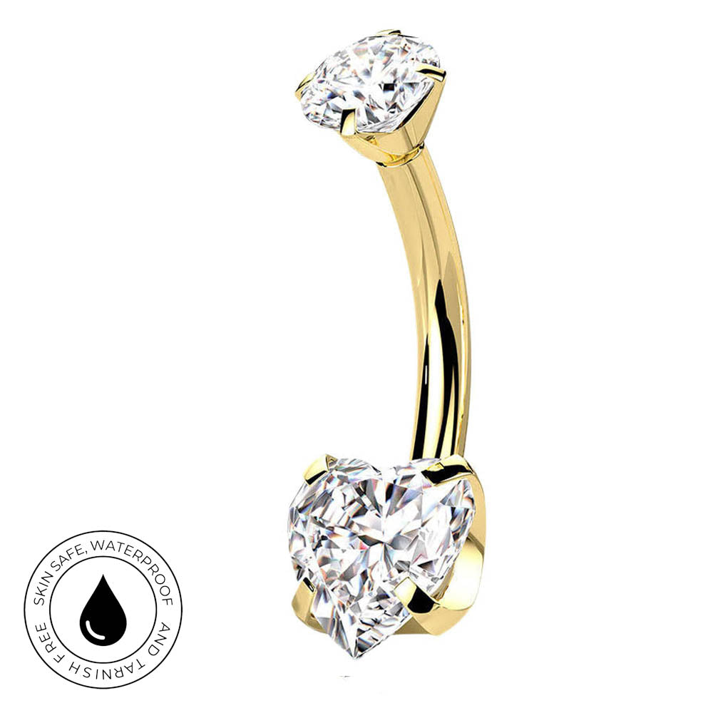 A curved yellow gold navel piercing ring with two clear gemstones, one round and one heart-shaped, shown on a white background with a circular skin-safe waterproof badge in the bottom-left corner.