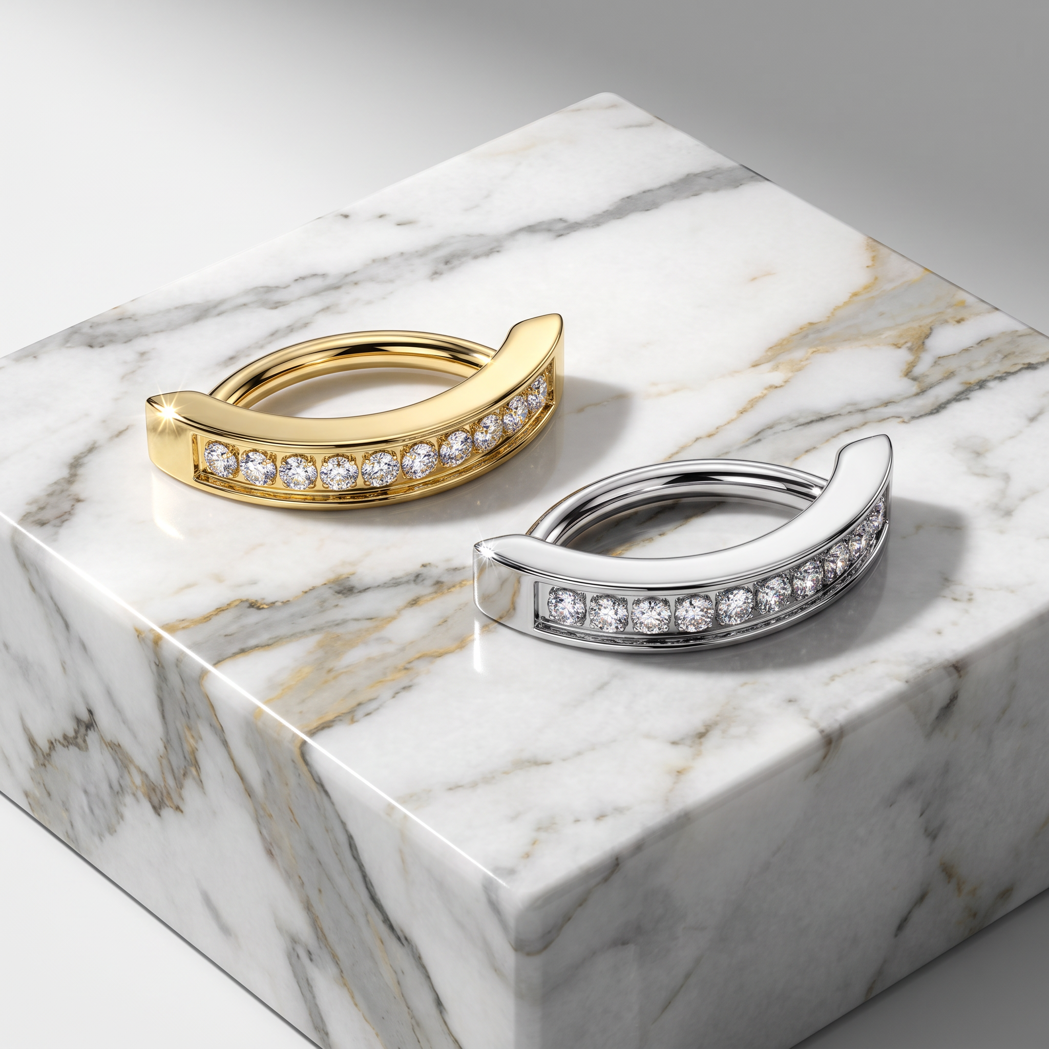 Two curved hoop-style earrings with rows of clear stones, shown in yellow gold and silver-tone metal, displayed on a white marble block against a light gray studio background.