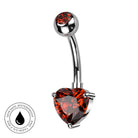 A curved barbell belly button ring with a polished silver-tone metal setting and a large faceted heart-shaped amber red gemstone at the bottom, shown on a plain white background with a circular skin-safe waterproof badge in the lower-left corner.