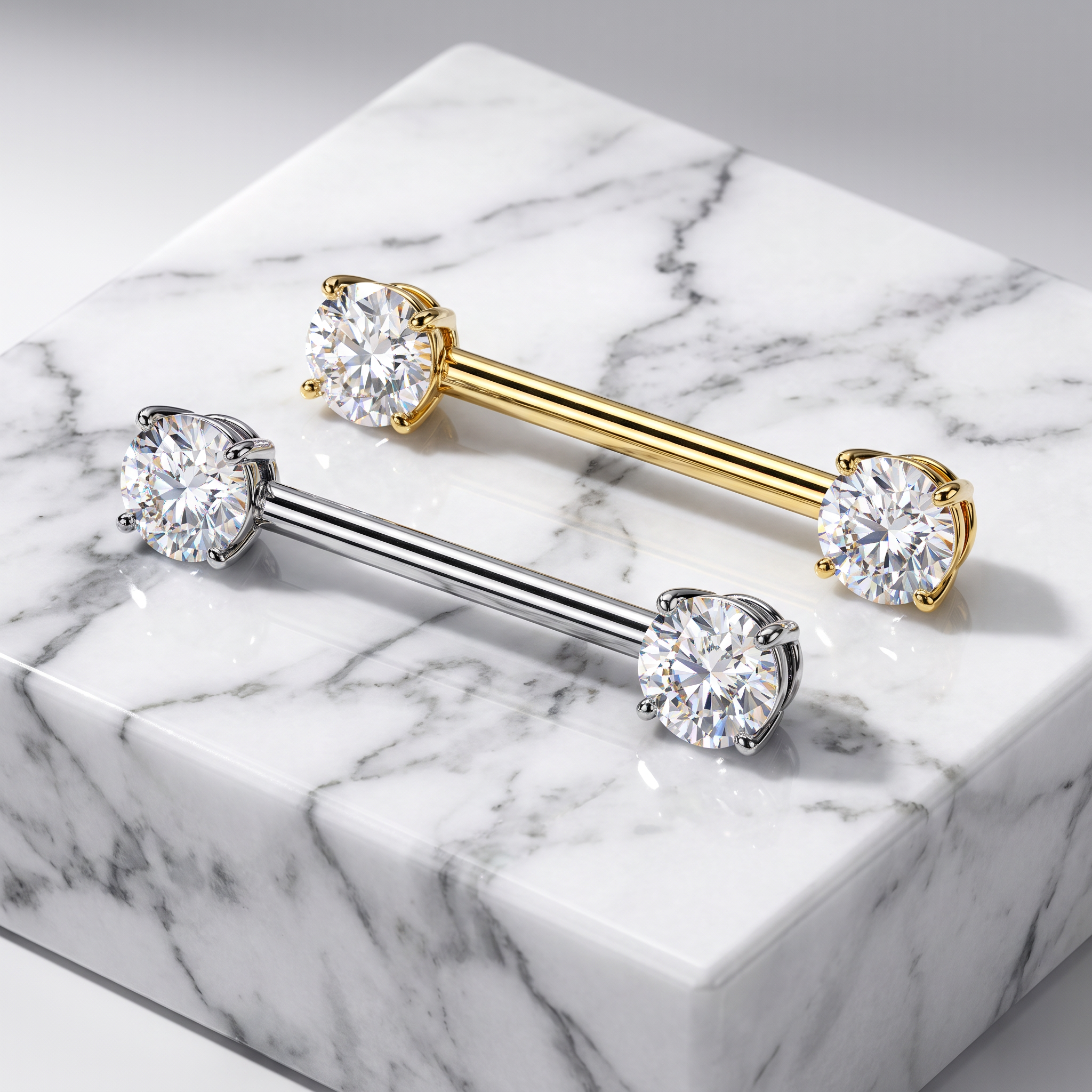 Two barbell-style body jewelry pieces with round clear gemstones at each end, one in yellow gold and one in silver, displayed on a white marble block.