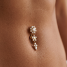 A gold-plated belly button ring with clear rhinestones, shown worn on a person's navel.