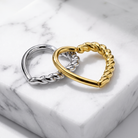 Two twisted rope-style metal rings, one polished gold and one polished silver, displayed on a white marble block.