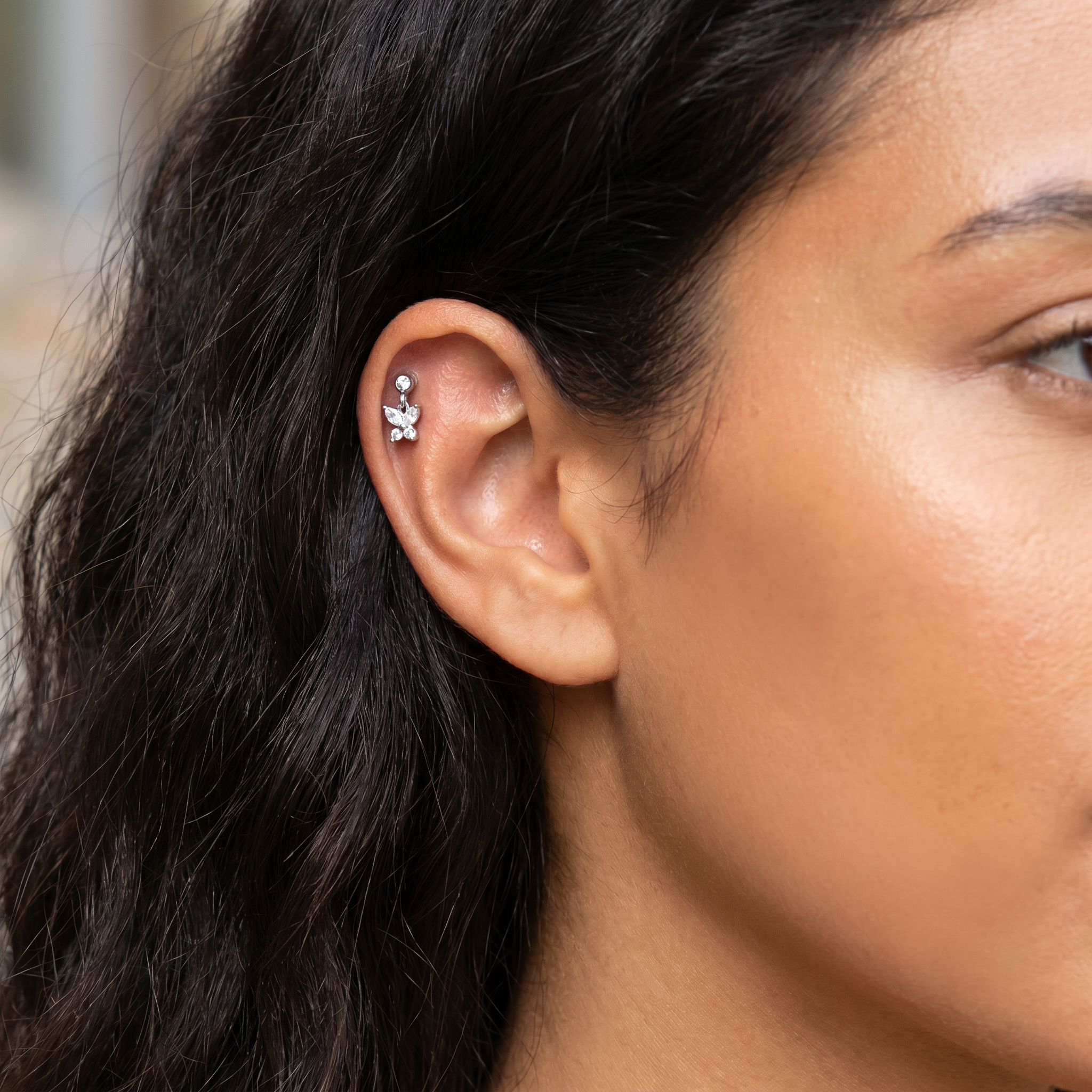 A close-up of a model's ear wearing a small silver ear cuff with a dangling floral design.
