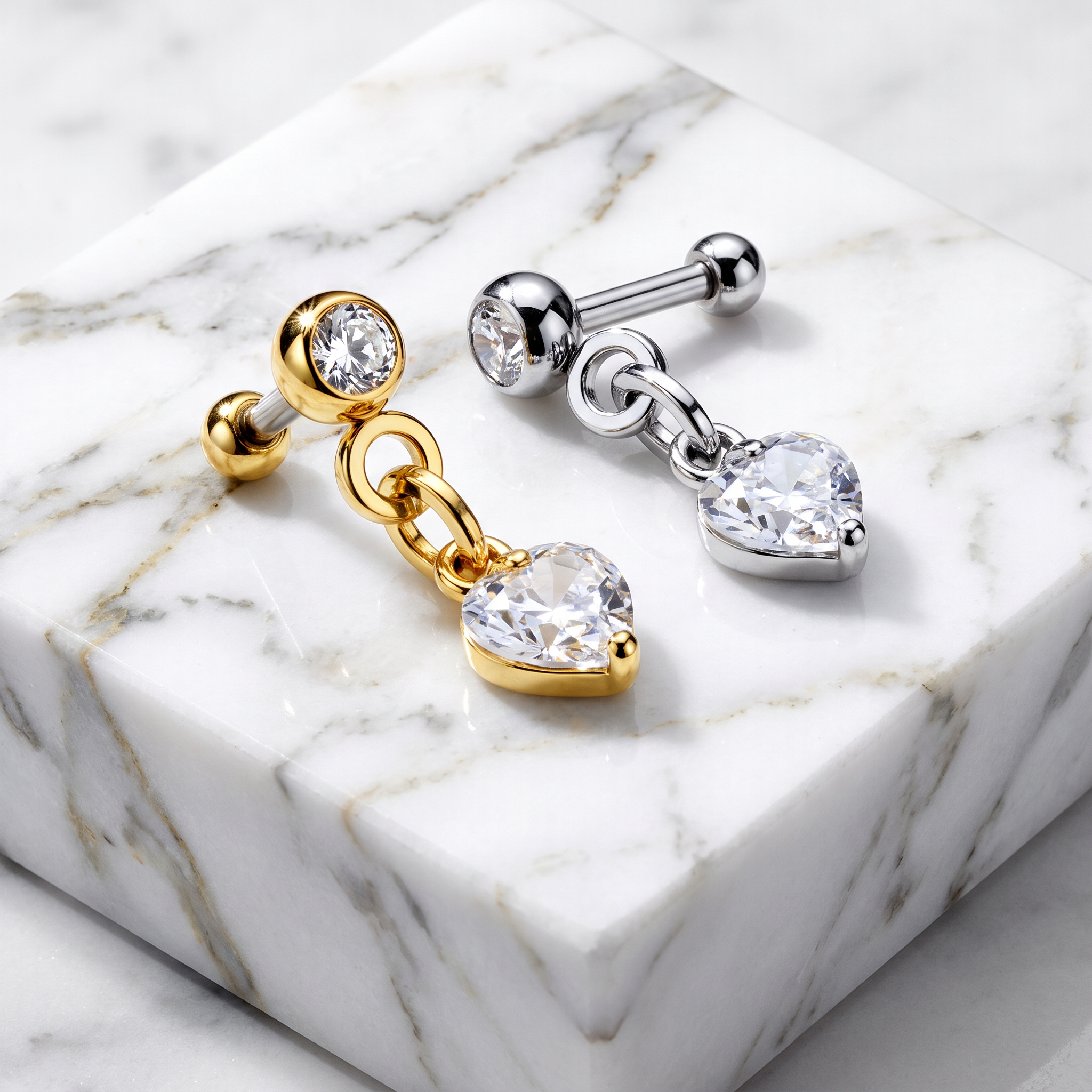 Two heart-shaped labret earrings displayed on a white marble block. One earring is gold-toned with a heart-shaped clear gemstone, and the other is silver-toned with a matching heart-shaped clear gemstone.