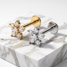 Two flower-shaped stud earrings displayed on a white marble block. One earring has a gold post and cluster, and the other has a silver post and cluster, both set with clear gemstones.