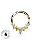 Gold-plated curved hoop piercing ring decorated with five marquise-cut clear gemstones, shown on a white background with a circular 'Skin Safe Waterproof' badge in the lower-left corner.