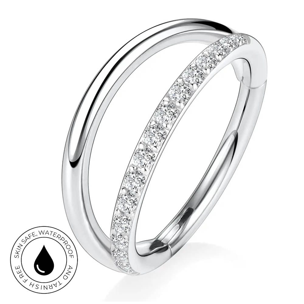 A silver-toned double-band ring with a channel-set row of clear cubic zirconia stones on the front band, shown on a white background with a small circular 'skin-safe waterproof' badge in the lower left.