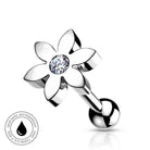 A silver-toned flower-shaped belly button ring with a clear faceted gemstone in the center and a ball end, shown on a white background with a small circular skin-safe waterproof badge.