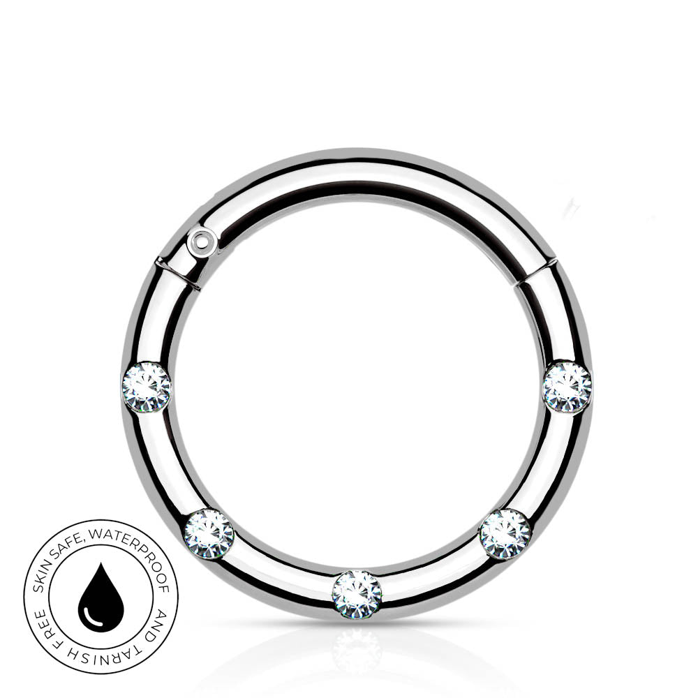 A silver-toned circular ring with five clear faceted gemstones spaced around the band, shown on a white background with a small circular 'skin-safe waterproof' badge in the lower left corner.