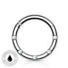A silver-toned circular ring with five clear faceted gemstones spaced around the band, shown on a white background with a small circular 'skin-safe waterproof' badge in the lower left corner.