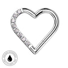 A silver-toned heart-shaped body jewelry clip with a row of clear rhinestones along one side, shown on a plain white background with a circular skin-safe waterproof badge in the lower-left corner.