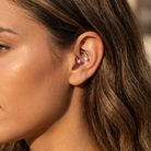 Close-up of a woman's ear wearing two small pink gemstone hoop earrings on her helix and upper ear cartilage.