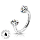 A silver-toned curved ring with two clear gemstones in a prong setting, shown on a white background with a small circular skin-safe waterproof badge in the lower left.