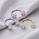 Three U-shaped ring ear cuffs displayed on draped satin fabric, featuring silver, yellow gold, and rose gold metal bands with clear gemstone settings and pink gemstone settings.