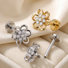 Four flower-shaped stud earrings displayed on a beige fabric surface, including two silver-toned and two gold-toned versions, each with clear rhinestone detailing and a straight post back.