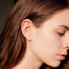 Close-up of a person's ear wearing a small silver hoop earring, with brown hair, soft lighting, and a blurred dark background.