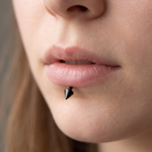 Close-up of a person's lower lip wearing a small black metallic cone-shaped lip piercing stud.