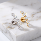 Two curved cluster stud earrings displayed on a white marble slab. One earring is silver-toned with clear stones, and the other is gold-toned with clear stones.