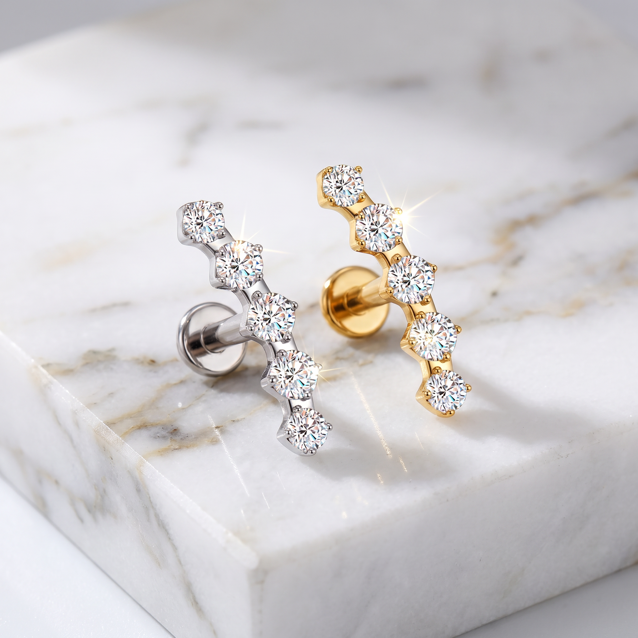 Two curved cluster stud earrings displayed on a white marble slab. One earring is silver-toned with clear stones, and the other is gold-toned with clear stones.