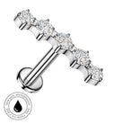 A silver-toned T-bar labret piercing stud with five round-cut clear gemstones, shown on a plain white background with a circular 'skin-safe waterproof' badge in the lower-left corner.