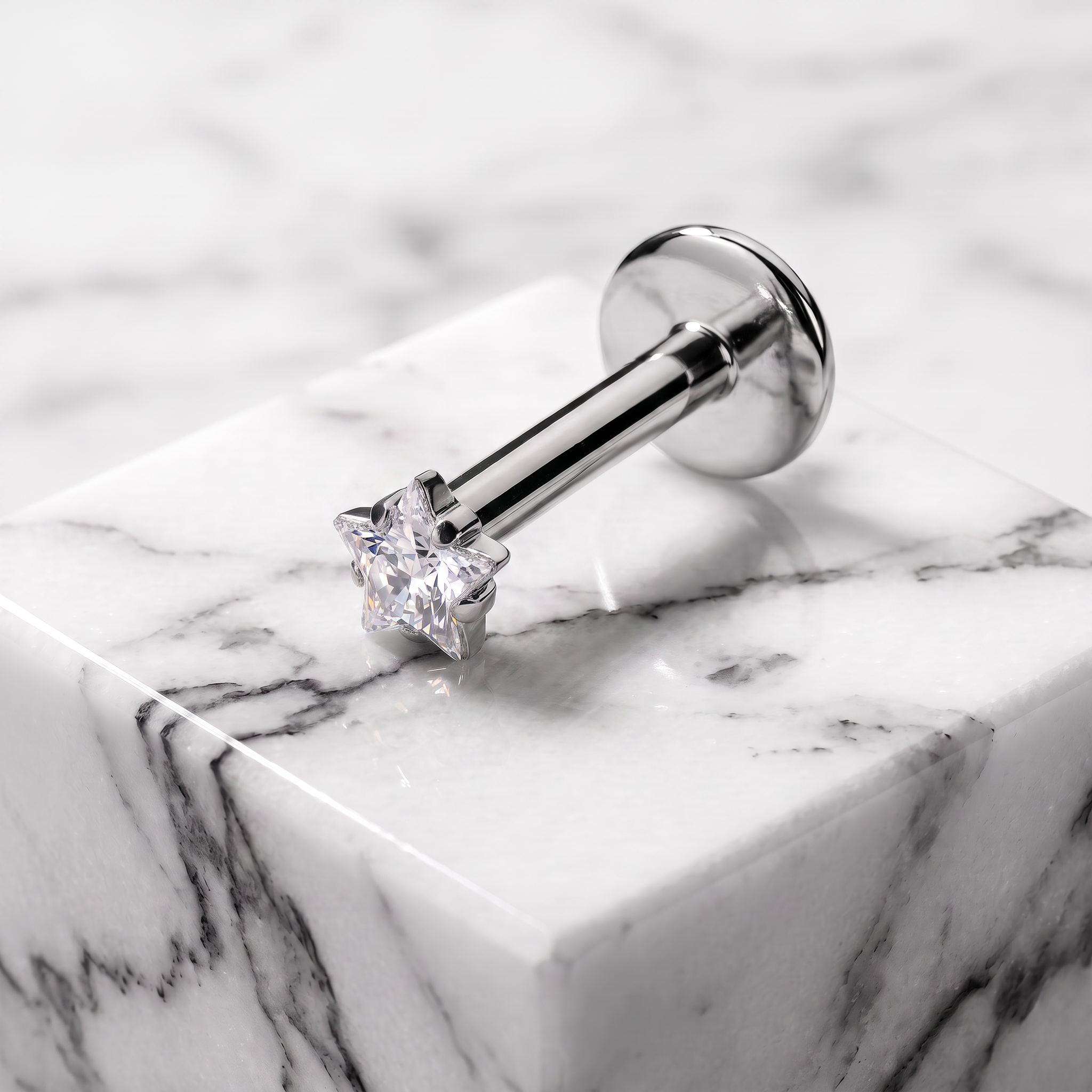 A silver-toned labret piercing stud with a clear gemstone, resting on a white marble block with gray veining.