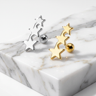 Two pairs of star-shaped stud earrings, one silver-toned and one gold-toned, displayed on a white marble block against a clean white background.
