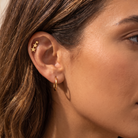 Close-up of a woman's ear showcasing a gold ear cuff with three stars and a small gold hoop earring.