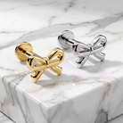 Two bow-shaped cufflinks, one in polished yellow gold and one in polished silver, displayed on a white and gray marble surface.
