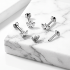 Four silver-toned barbell stud earrings with heart-shaped crystal clusters, arranged on a white marble slab.