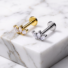 Two butterfly-shaped stud earrings displayed on a white marble block. One earring has a gold-toned metal body with clear marquise and round crystals, and the other has a silver-toned metal body with matching clear crystals.