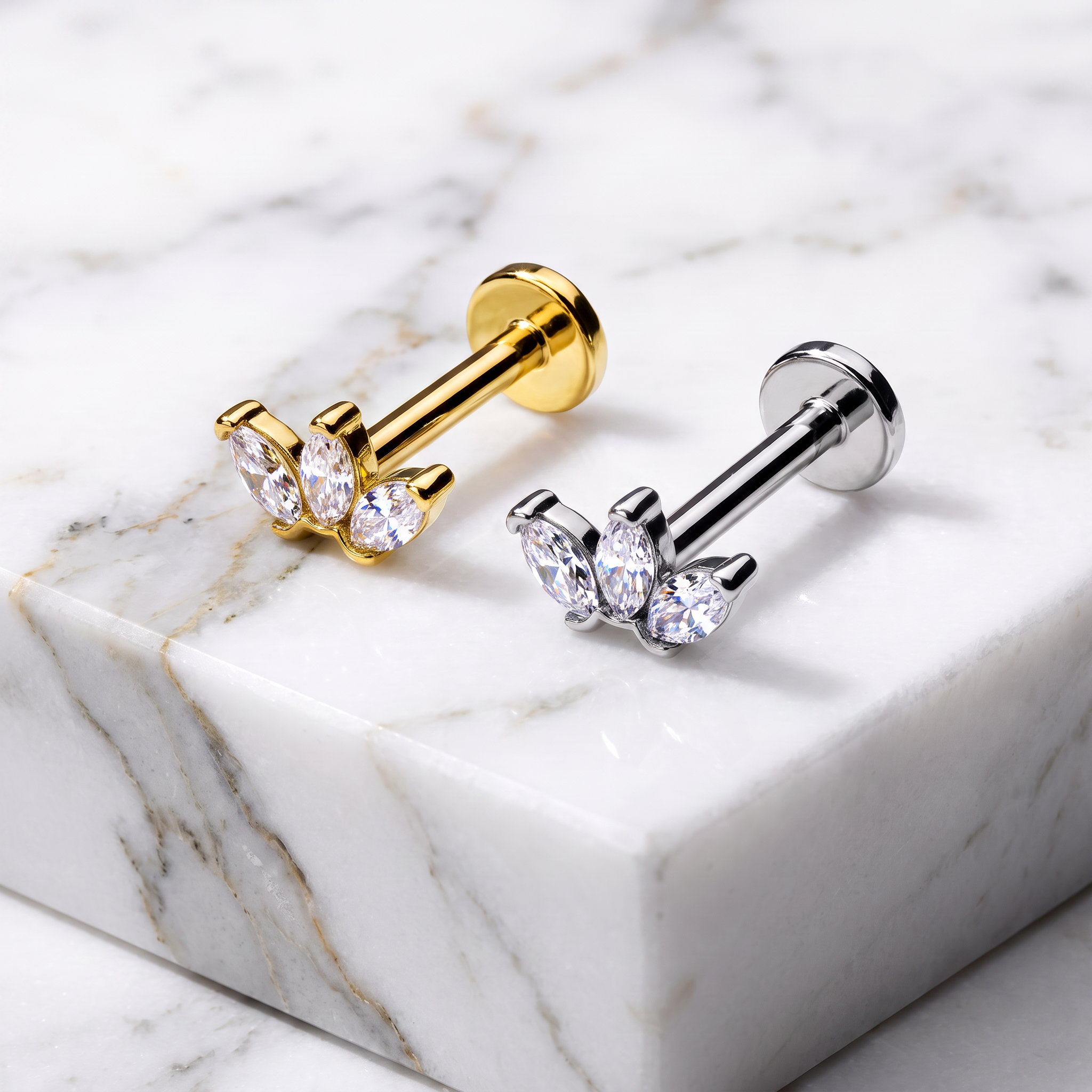 Two butterfly-shaped stud earrings displayed on a white marble block. One earring has a gold-toned metal body with clear marquise and round crystals, and the other has a silver-toned metal body with matching clear crystals.
