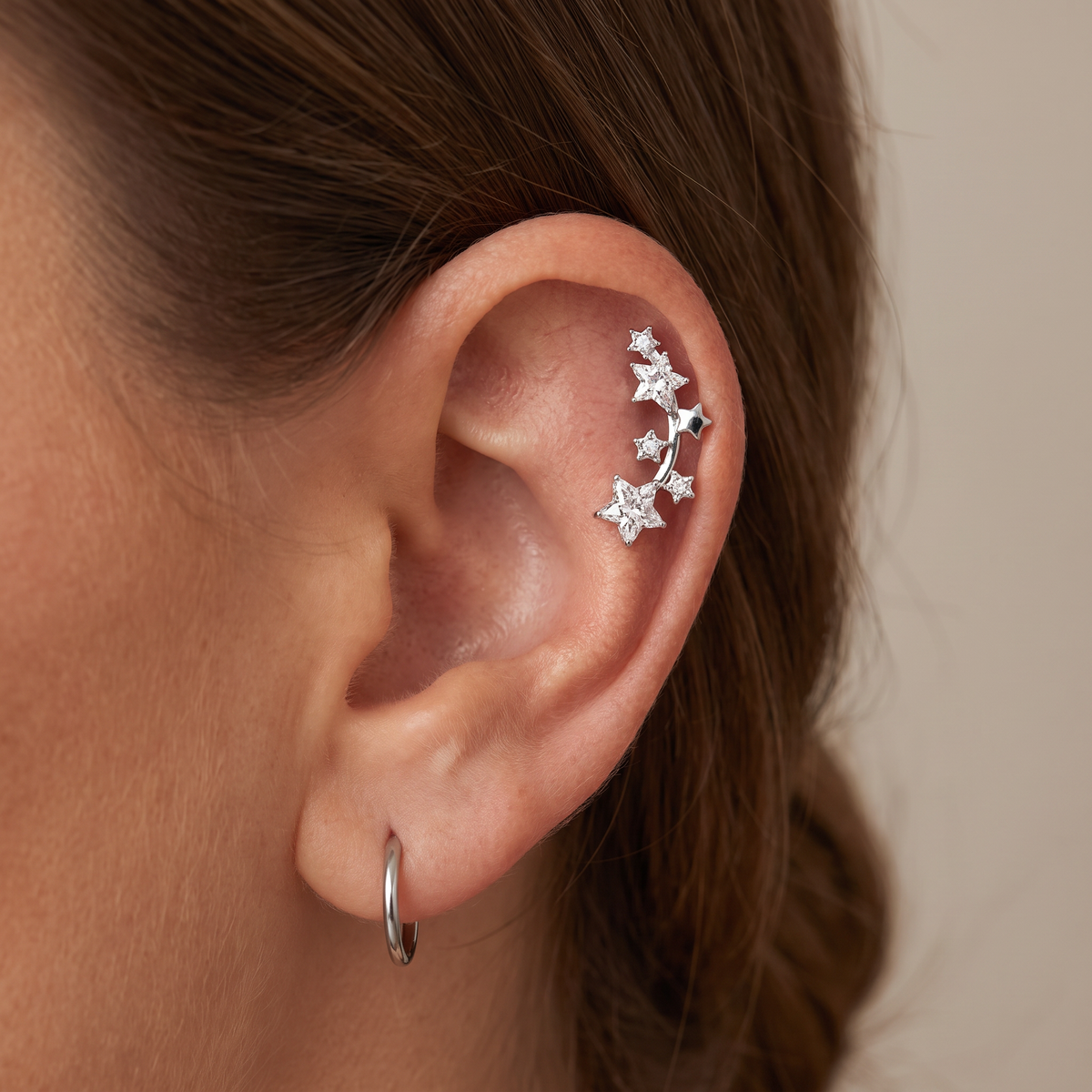 A close-up of a person's ear showcasing a silver ear cuff adorned with small star-shaped crystals, alongside a simple silver hoop earring.
