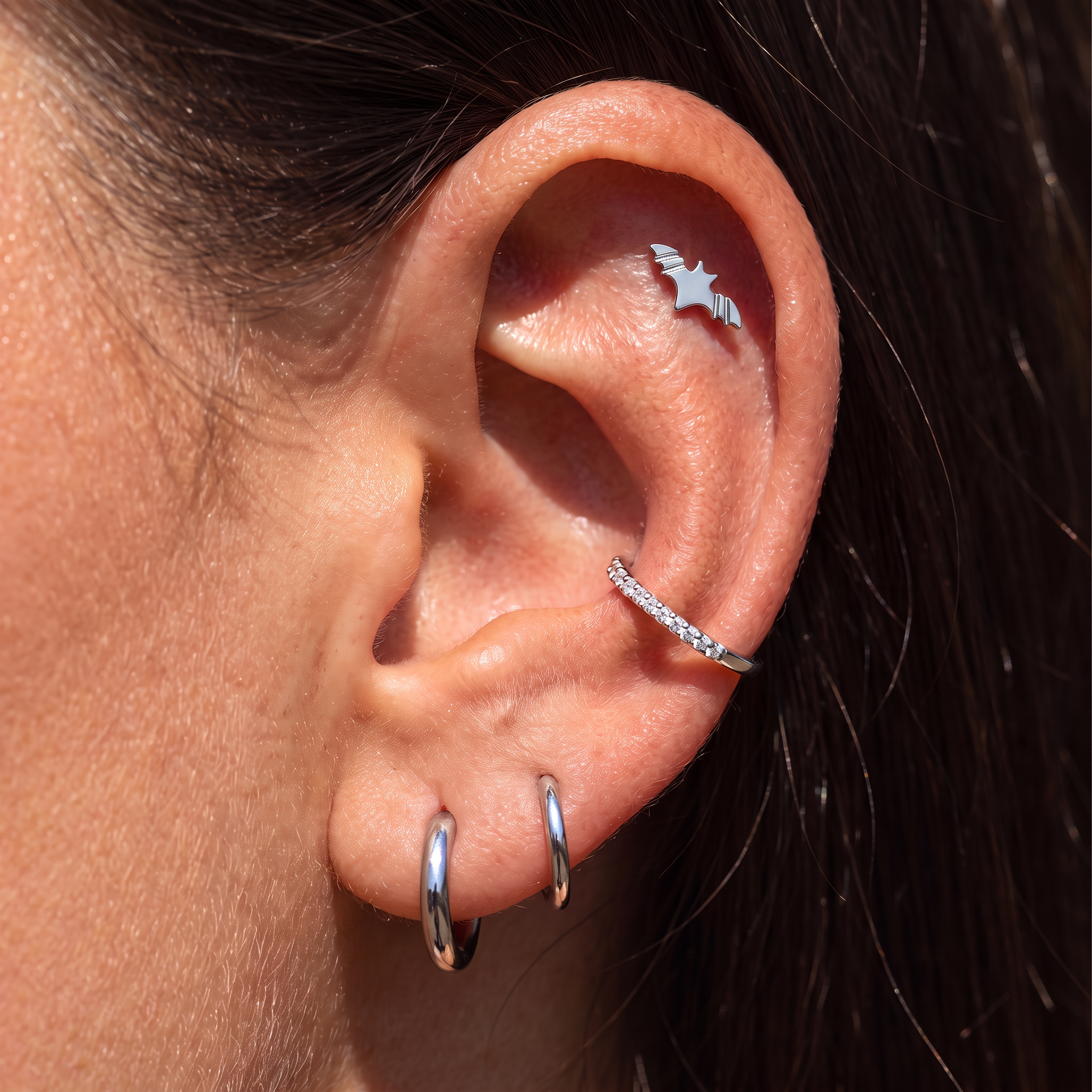 Close-up of a person's ear showcasing multiple silver cartilage piercings, including two small hoop earrings in the lobe, a curved barbell piercing on the helix, and a star-shaped piercing on the upper ear cartilage.