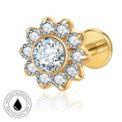 A gold flower-shaped stud earring with a central round clear gemstone surrounded by a halo of smaller clear stones, shown on a white background with a small circular skin-safe waterproof badge in the lower left corner.